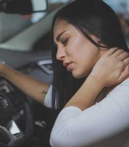 Photo of a woman in a car holding the back of her neck